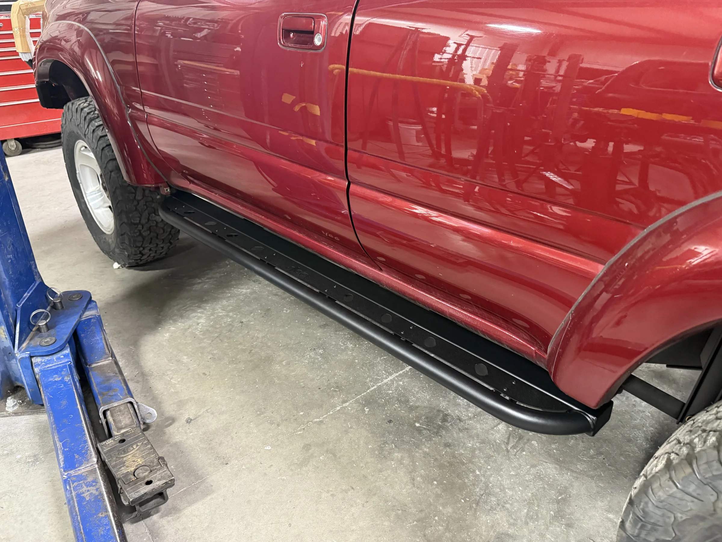 Slee rock sliders installed beneath the doors of the red 80 Series Land Cruiser