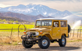 A perfectly restored yellow FJ40. A 1977 Stage 3 Patina Restoration parked on a dirt road with mountains and green grass in the background. Resurrection Land Cruisers